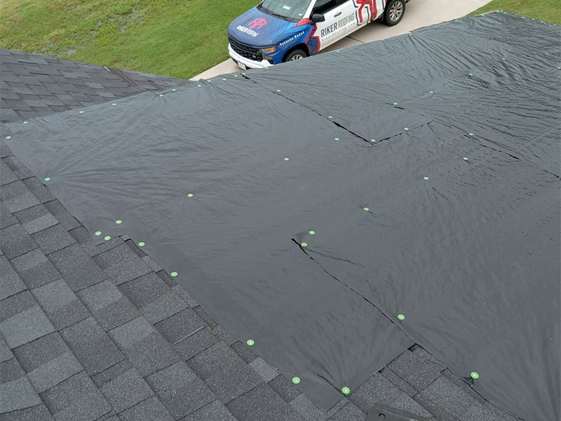 Roof covered with a tarp after storm damage with Riker Home Services truck in the background